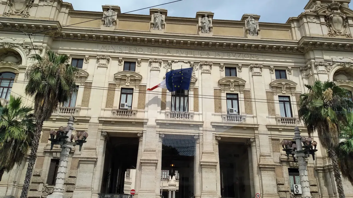 Ingresso di un palazzo storico con le bandiere italiana ed europea e la scritta Ministero della Pubblica Istruzione