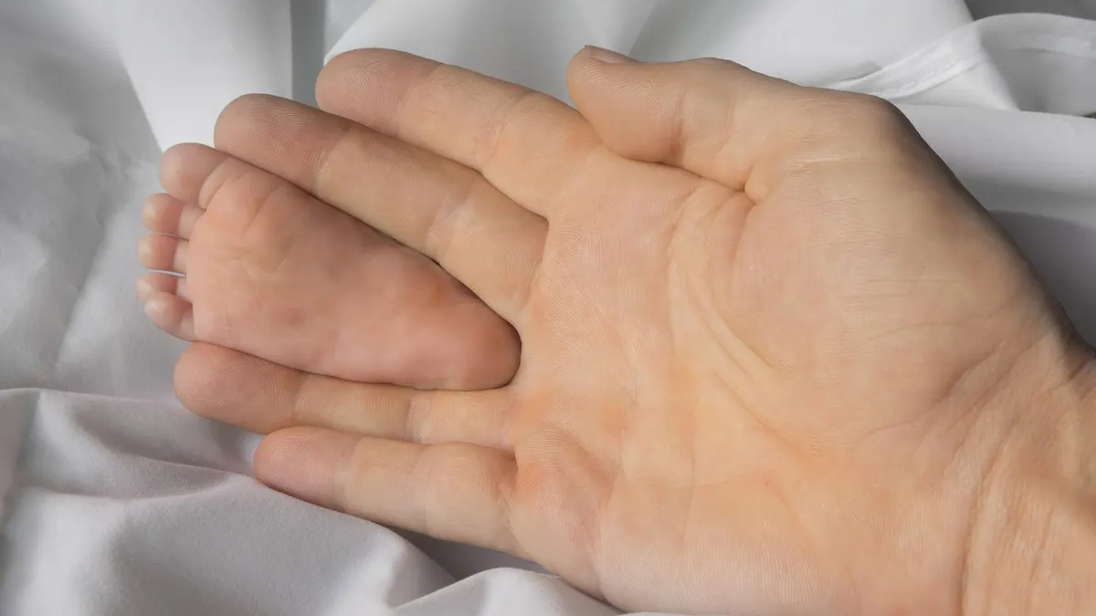 Il piede di un neonato tra le dita di una mano adulta