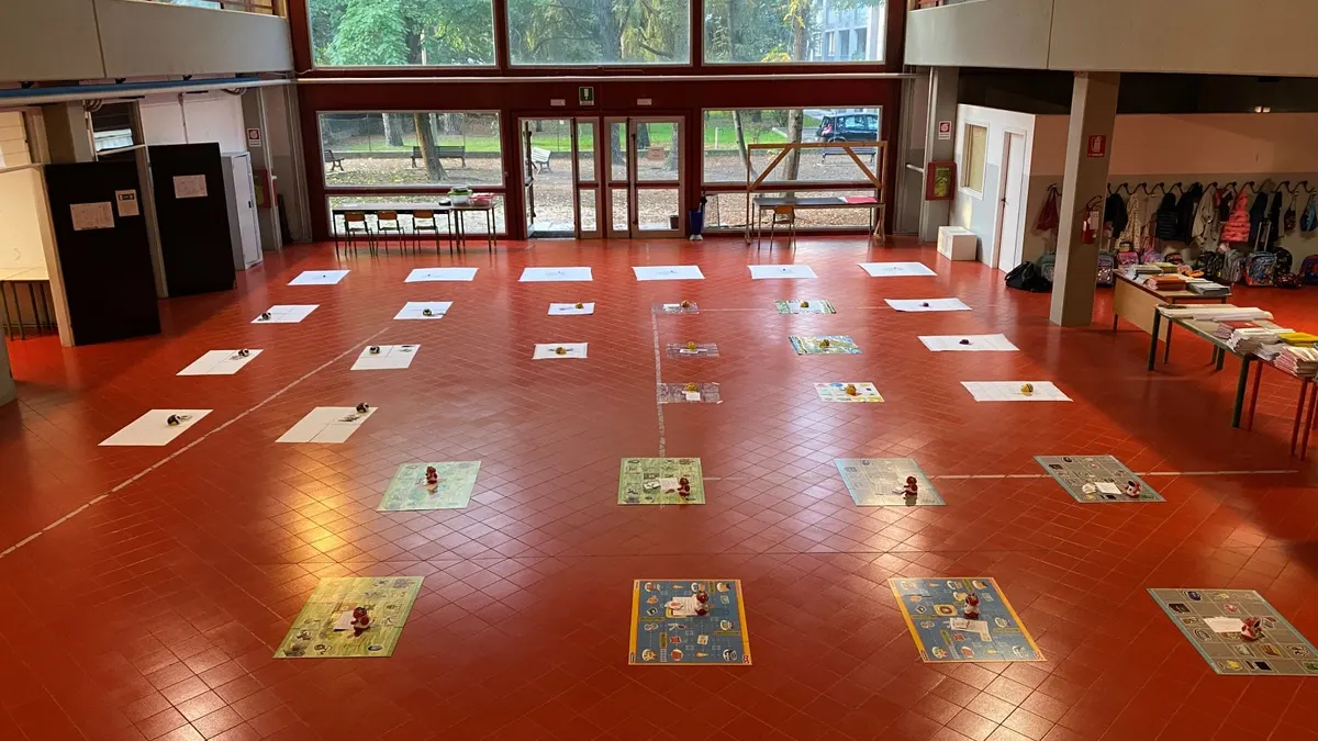 Ampio atrio di una scuola con grandi vetrate, pavimento rosso e giochi didattici sul pavimento