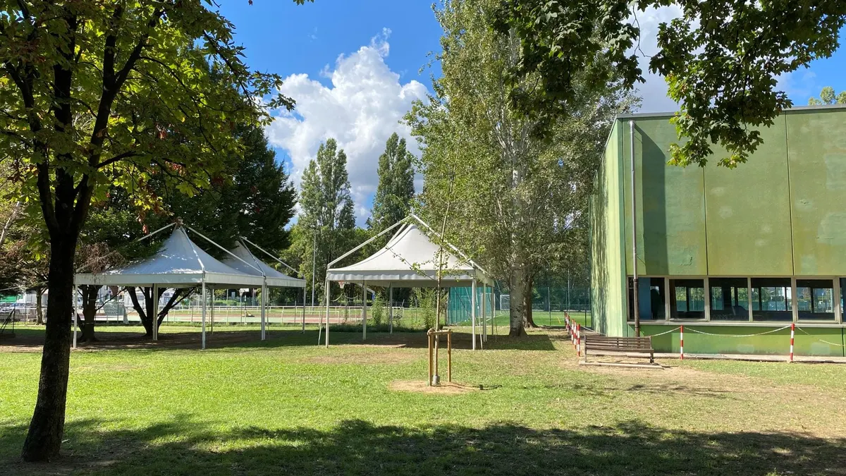 Giardino di una scuola con due gazebo bianchi, una panchina e l'edificio scolastico