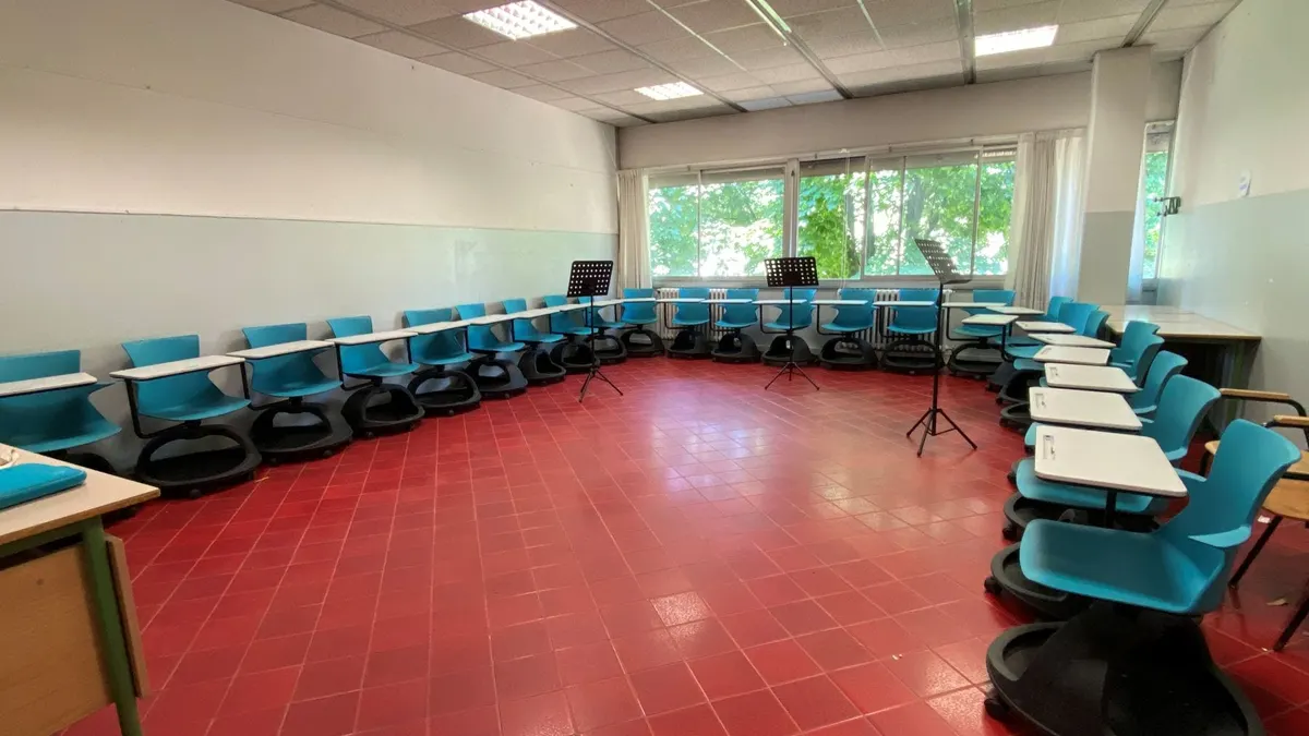 Aula con sedie azzurre su rotelle disposte a semicerchio e leggii